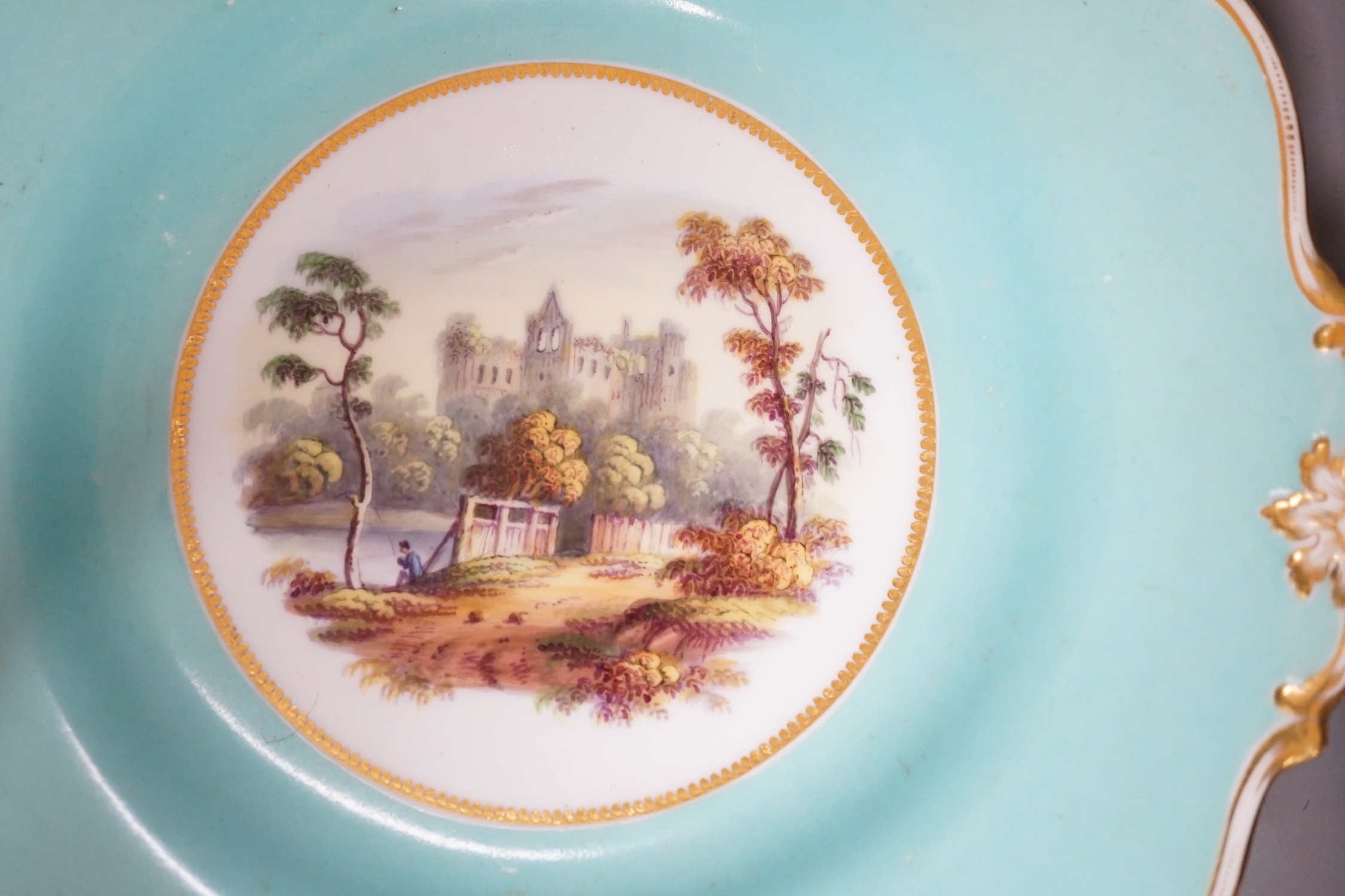 A pair of English porcelain plates with moulded white and turquoise borders both painted with landscapes, one titled in Guildford, diameter 22.5cm
